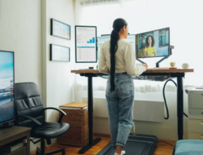 A woman stands on a treadmill, typing on a laptop while exercising.