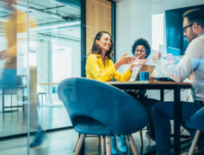 A group of diverse individuals seated around a table in a modern office setting, engaged in discussion.