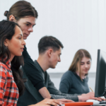 Top 10 Computer Skills Everyone Should Learn in 2025 Four individuals working at computers in a classroom.