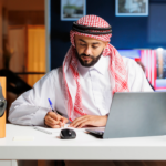 Arab man working on laptop in a cozy, well-lit home.