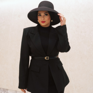 A woman wearing a black suit and hat stands confidently, exuding professionalism and elegance.