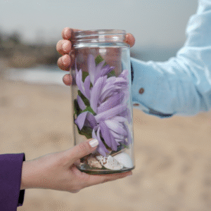 A person holding a jar filled with vibrant purple flowers, showcasing a delicate floral arrangement.